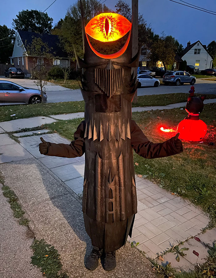 Child wearing a creative kids Halloween costume with a glowing eye helmet and dark armor standing outdoors at dusk.