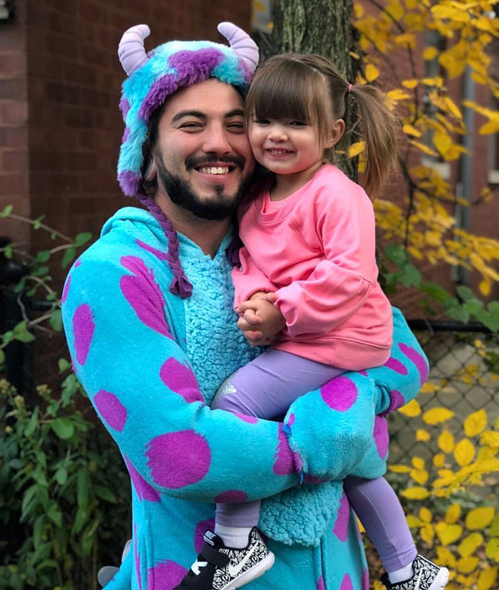 Man in a colorful monster costume holding a smiling little girl, showcasing creative kids' Halloween costume ideas outdoors.