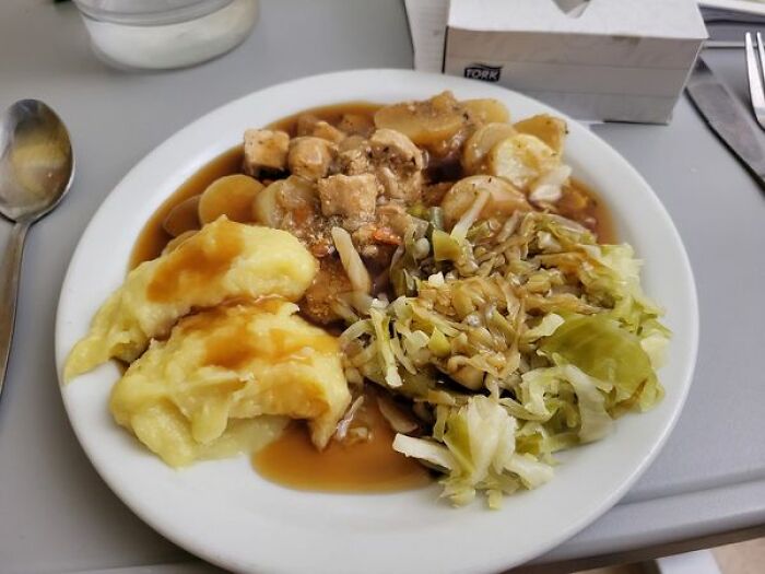 Hospital food plate with mashed potatoes, cooked vegetables, and meat in brown gravy served on a white dish.