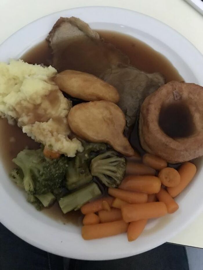 Plate of hospital food with mashed potatoes, gravy, roast meat, vegetables, Yorkshire pudding, and baby carrots meal example.