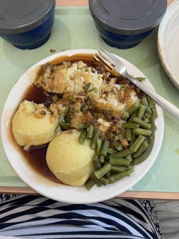 Hospital food example showing mashed potatoes, green beans, and meat pie with gravy served on a tray with drinks.