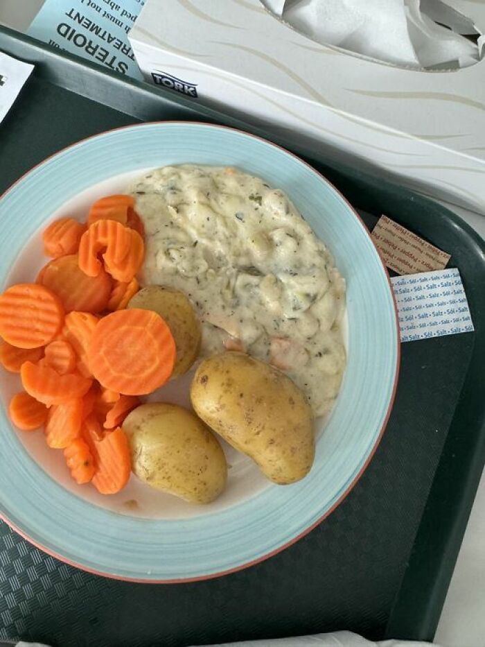 Plate of hospital food with boiled potatoes, sliced carrots, and creamy vegetable stew on a hospital tray.
