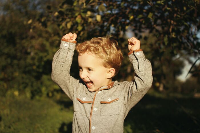 Young boy outdoors raising hands excitedly, illustrating joy and wonder related to mind-blowing coincidences.