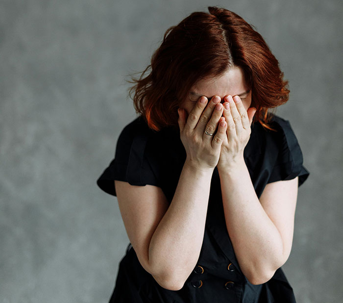 Woman with red hair covering her face, expressing shame and heartbreak in a moment that turned friends to strangers.