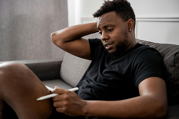 Man sitting on a couch looking ashamed and distressed while holding a pen, reflecting on moments that turn friends to strangers.