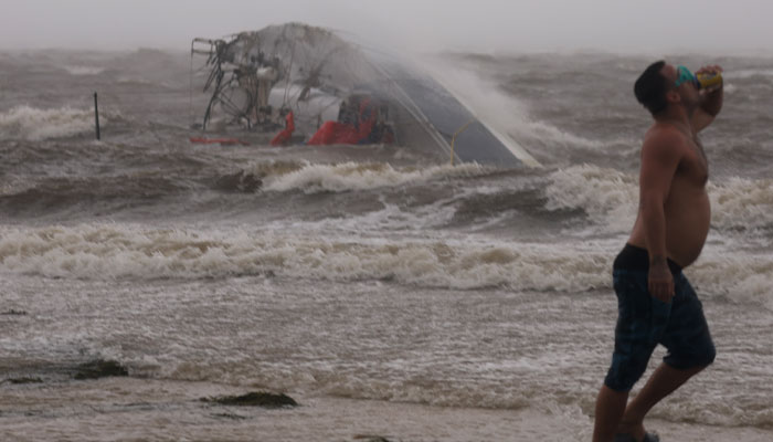 A Man Has A Drink While A Capsized Boat Washes Ashore