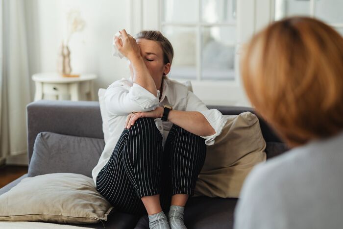 Woman sitting on couch, covering her face with hand, expressing distress during a conversation about toxic relationships and red flags.