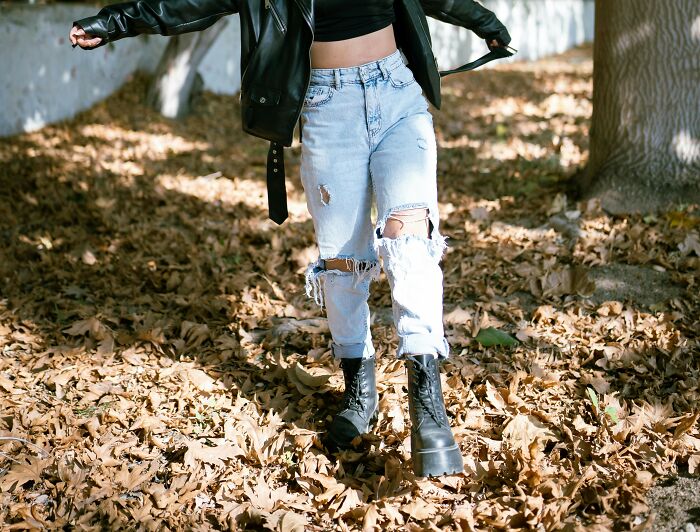 Person wearing ripped jeans and black boots walking through autumn leaves, showcasing trends that disappeared quickly.