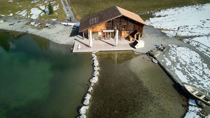 A wooden cabin by a lake with clear water and snow patches, showcasing a mind-blowing coincidence in nature.