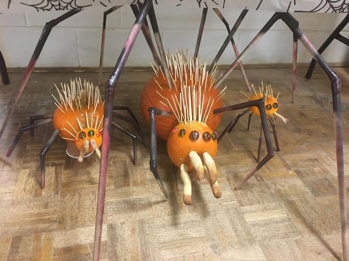 Pumpkin carvings transformed into quirky spider designs with toothpick spines and painted legs on a wooden floor.