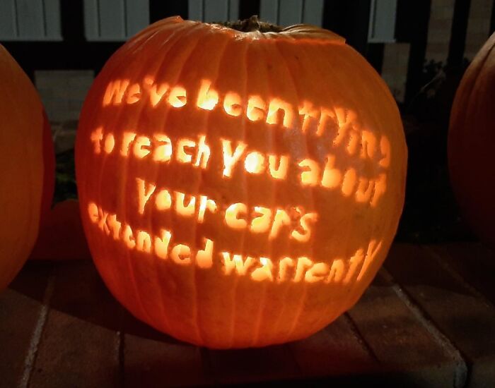 Pumpkin carving with a humorous message about car warranty glowing warmly in a dark outdoor setting.