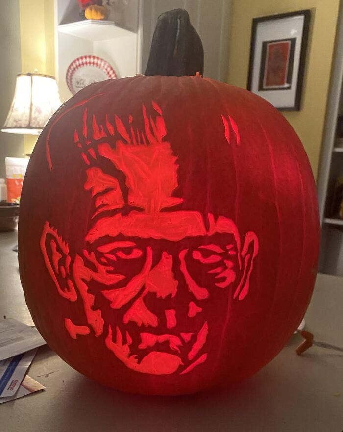 Carved Frankenstein face pumpkin glowing red indoors, showcasing spooky and charming pumpkin carvings for Halloween.