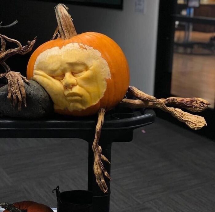 Pumpkin carving with a detailed face sculpture showing a sleeping expression, surrounded by twisted branch-like decorations.
