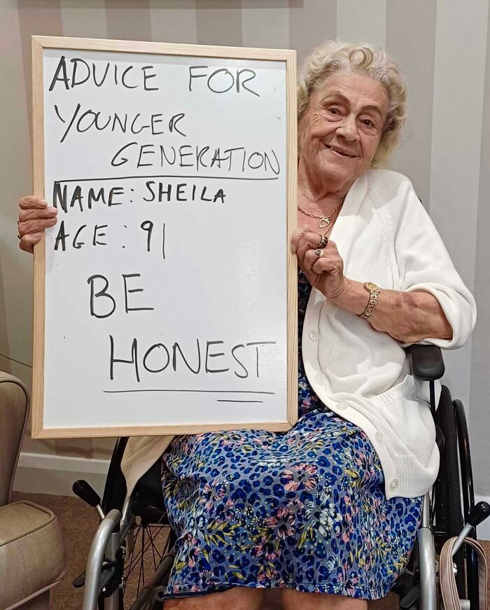 Elderly woman in wheelchair holding sign with life advice for younger generation focused on honesty.