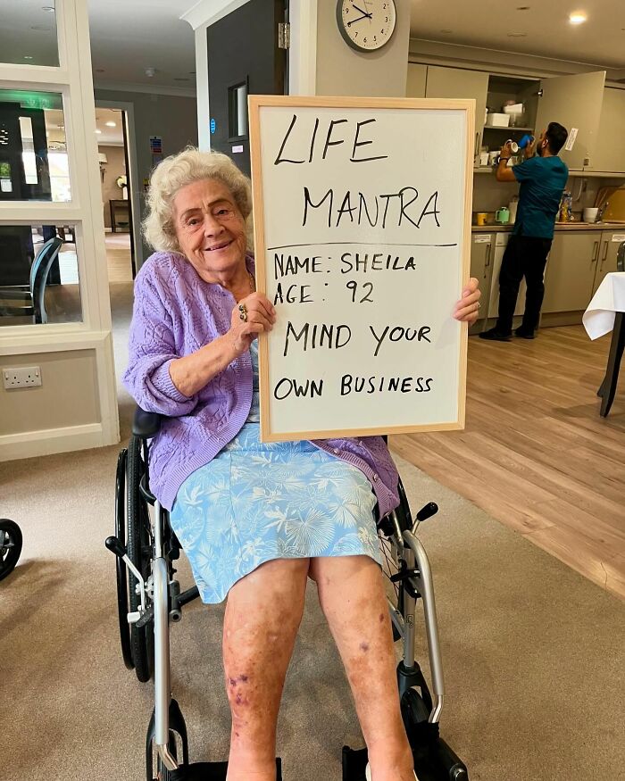Elderly woman in wheelchair holding life advice board with mantra from elders doling out life advice.
