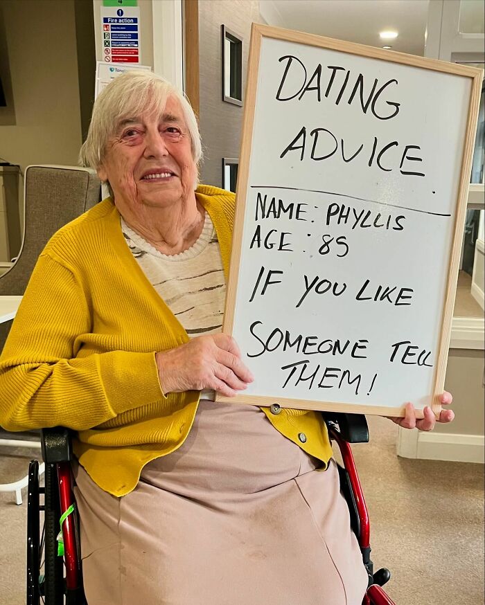 Elderly woman in a yellow cardigan sharing dating advice on a whiteboard for elders doling out life advice Instagram page.
