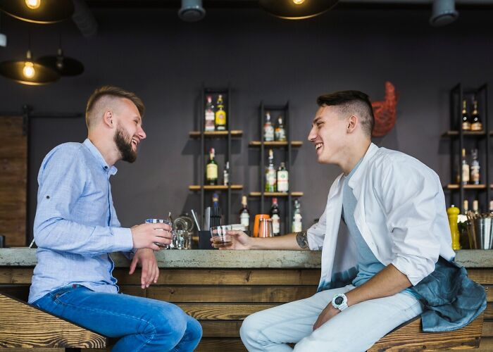 Two young men enjoying drinks and laughing at a bar, illustrating mind-blowing coincidences between friends.