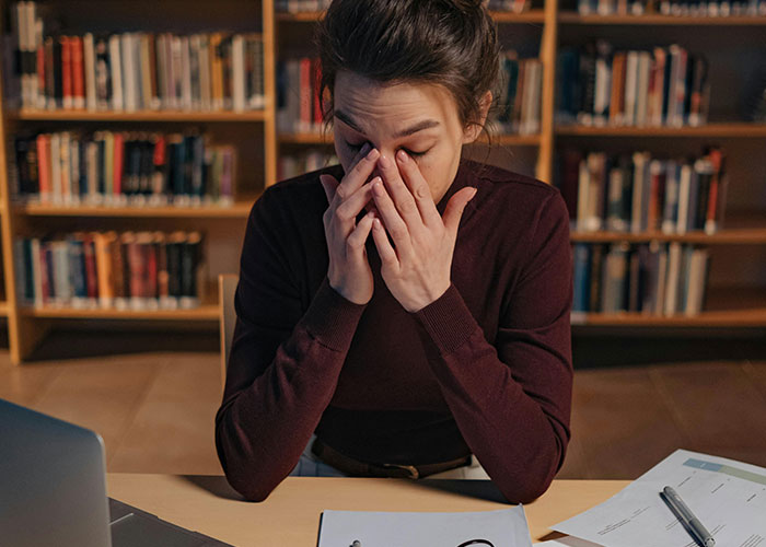Person in a library rubbing eyes tiredly, representing indicators of a super smart person who hides it well.