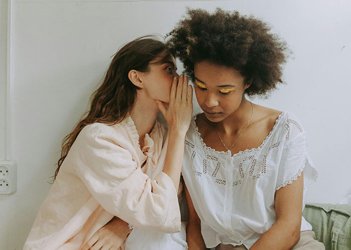 One person whispering a secret to another, illustrating indicators the person you’re talking to is super smart and hides it well.