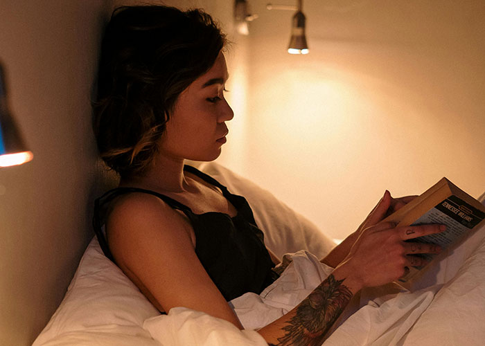 Woman reading a book in bed, showing quiet focus and traits of a person who is super smart and hides it well.