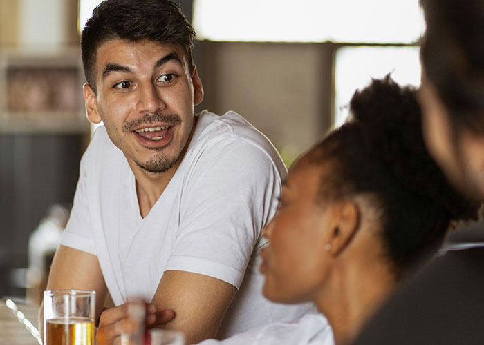 A man showing signs of being super smart and hiding it well while engaging in a lively conversation with others.