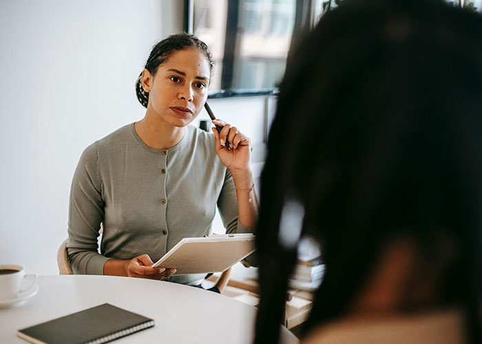 Woman attentively listening and taking notes, showing indicators of a person who is super smart and hides it well.