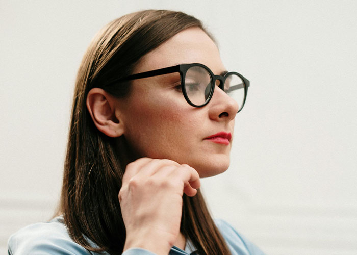 Woman wearing glasses with a thoughtful expression, showing signs of being super smart and hiding it well.