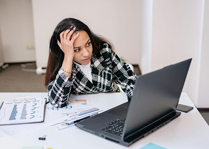 Woman analyzing data on laptop, showing signs of being super smart and hiding intelligence well in an office setting.