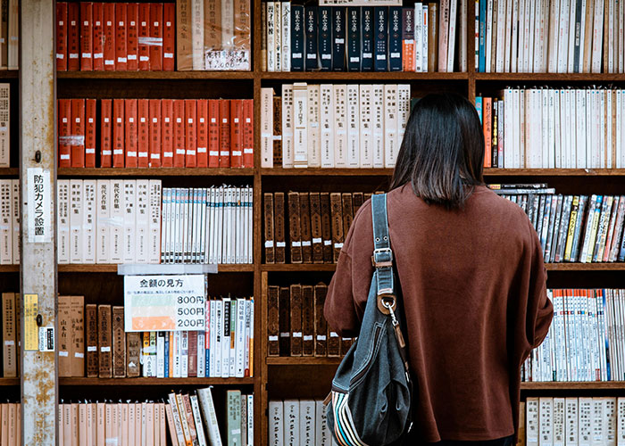 Person in a brown sweater browsing books on a library shelf illustrating indicators of a super smart person who hides it well