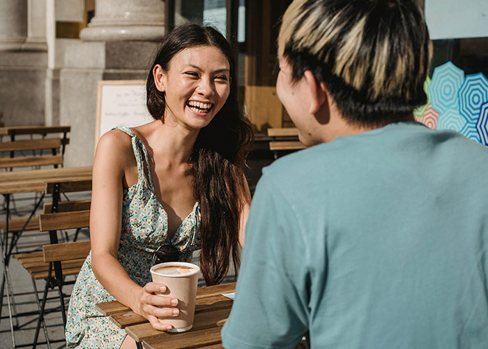 Two people having coffee outdoors, showing indicators of a person who is super smart and hides it well.