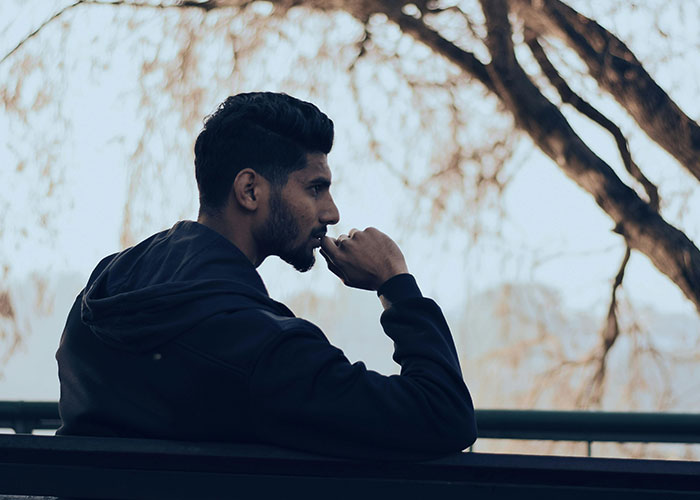 Man sitting on a bench outdoors, looking thoughtful, representing indicators of a super smart person who hides it well.
