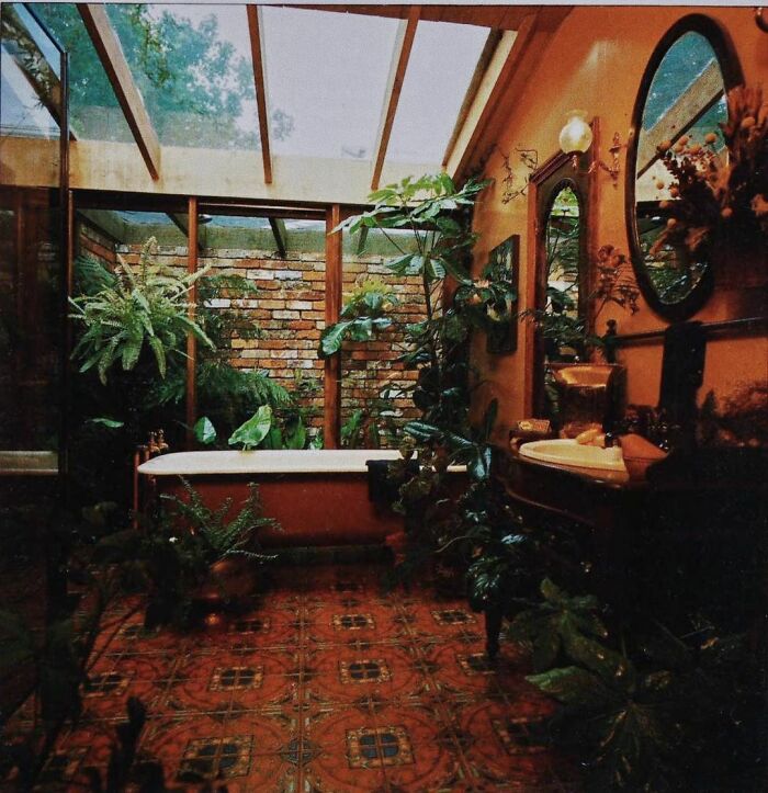 Vintage bathroom interior from the ’50s to ’80s featuring a clawfoot tub, lush plants, and patterned tile floor.