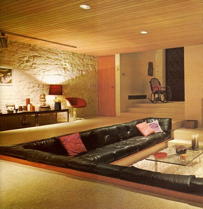 Mid-century modern living room with sunken black leather sofa and vintage decor from 50s to 80s interiors.
