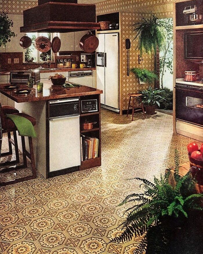 Vintage kitchen interior from the 70s with patterned flooring, wood cabinetry, hanging pots, and lush green houseplants.