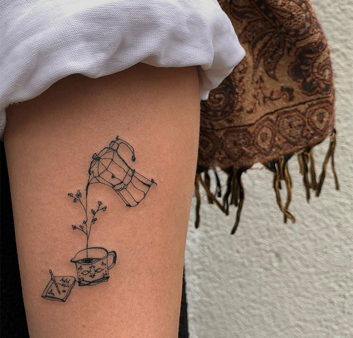 Small tattoo of a hand watering a plant in a cup, symbolizing growth and creativity.