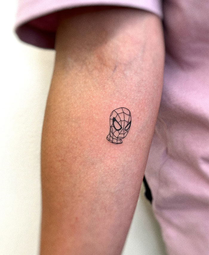 Small tattoo of a superhero mask on an arm, showcasing minimalist design with intricate linework.