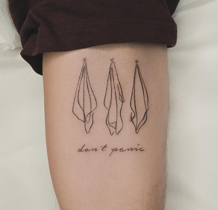 Small tattoo featuring three hanging towels and the phrase "don't panic" on an arm.