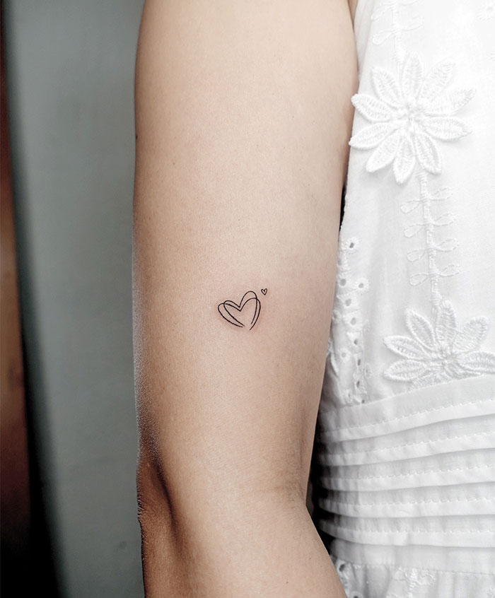 Minimalist small tattoo of a heart on an arm, showcasing simple yet impactful design.