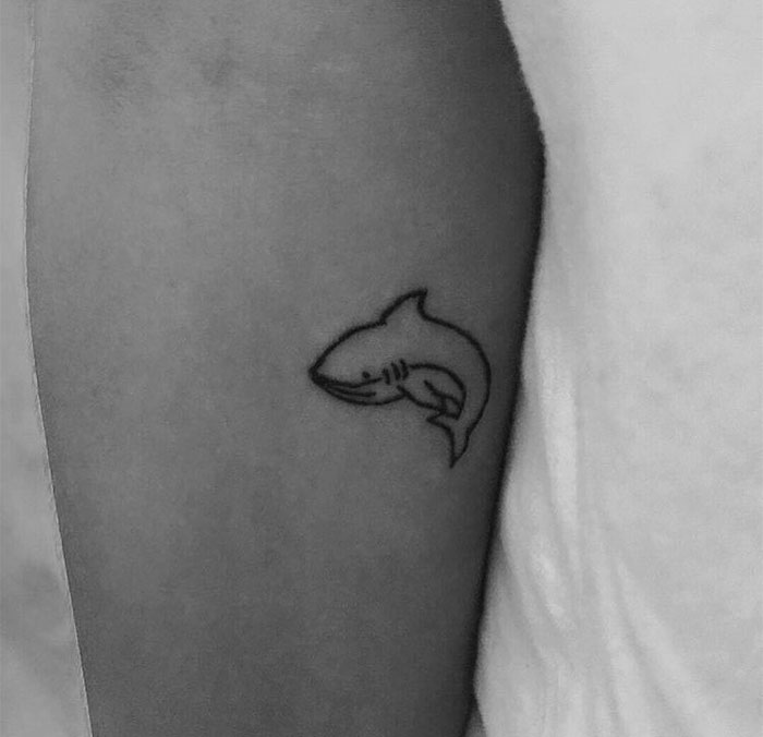 Small shark tattoo on upper arm, showcasing a minimalist and impactful design.