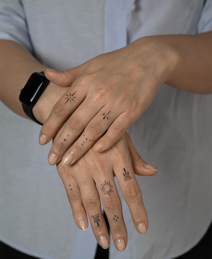 Minimalistic small tattoos on hands, featuring geometric and star designs.