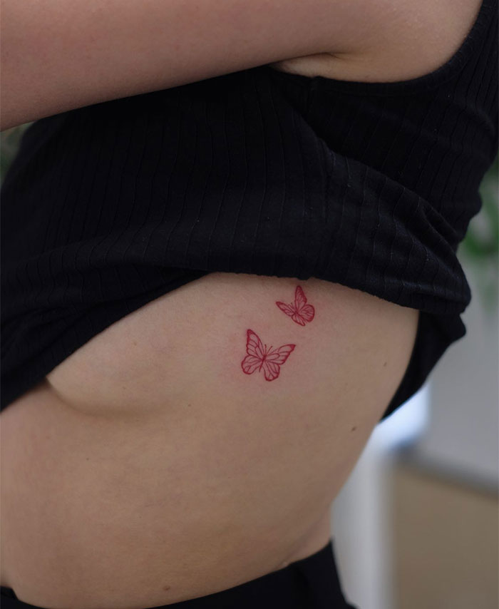 Small tattoo of two red butterflies on a person's side, showcasing intricate detail and vibrant color.