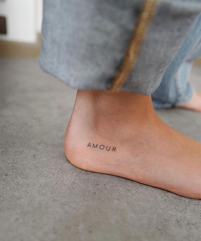 Small tattoo reading "Amour" on the ankle, showcasing minimalist tattoo ideas.