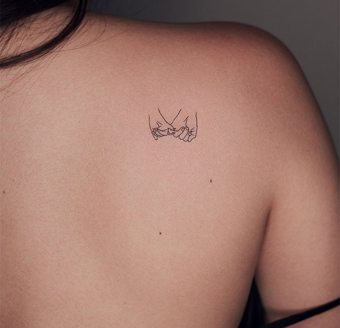 Minimalist small tattoo of two pinky-promising hands on a person's back.