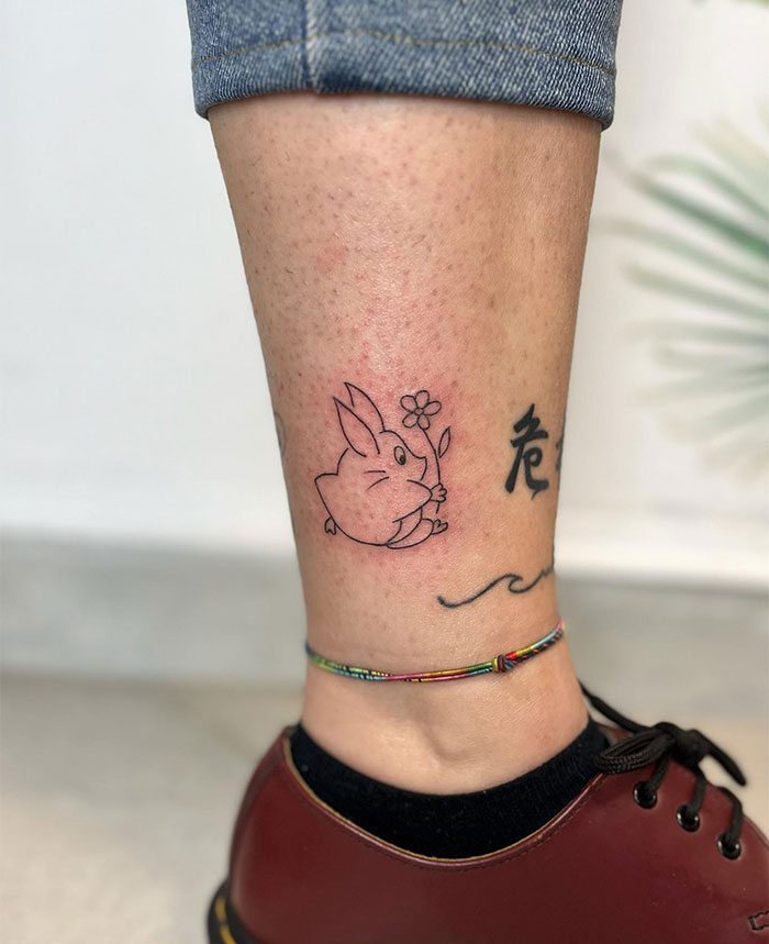Small tattoo of a cute bunny holding a flower on a person's leg, alongside kanji characters, showcasing creative tattoo ideas.