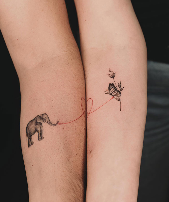 Small tattoo with an elephant and butterfly connected by a red thread on arms.
