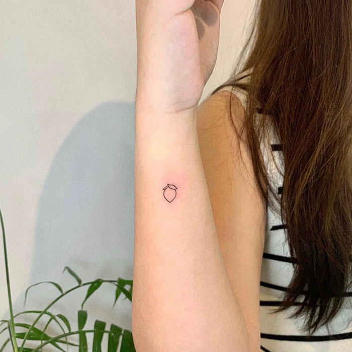Minimalist small tattoo of an acorn on a woman's forearm, showcasing impactful tiny tattoo design.