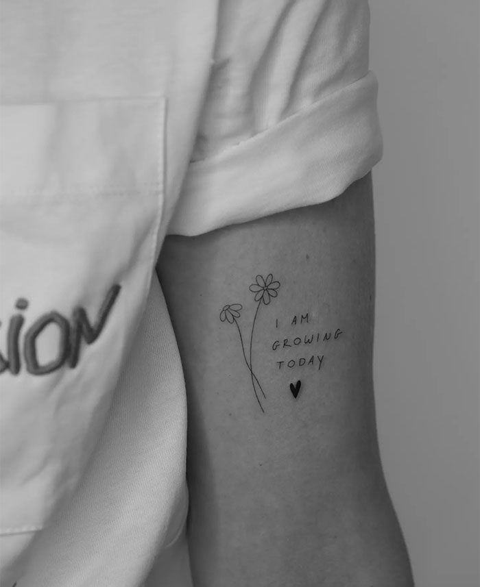 Small tattoo of flowers with "I am growing today" text, emphasizing personal growth.
