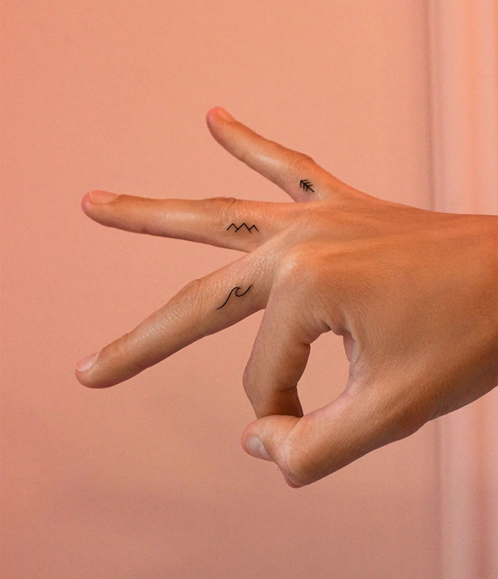 Minimalist small tattoos on fingers, featuring mountain, wave, and arrow designs.