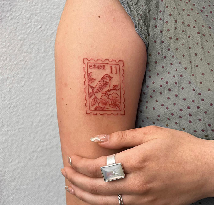 Small tattoo of a vintage Japanese stamp with a bird design on an arm.