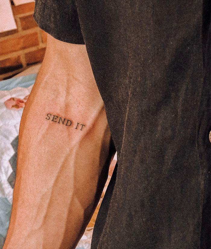 Close-up of a small tattoo reading "SEND IT" on a person's arm.